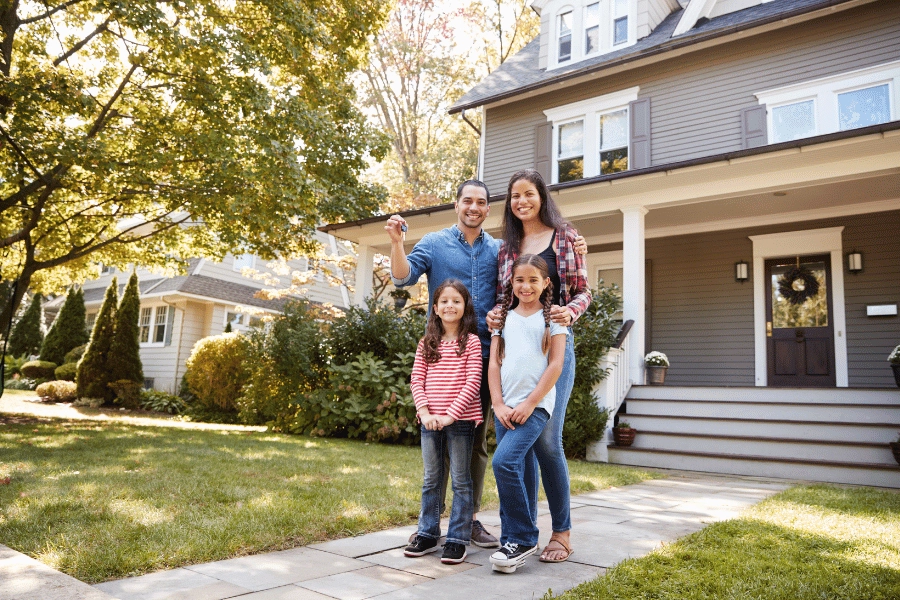 cute family of four holding keys up in front of new suburban home with a front porch